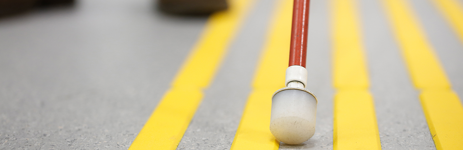 A plastic tipped cane with red tape serves as a tool to help an individual cross the street
